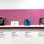 Vier Fotobücher auf einem Regal vor pinker Wand.